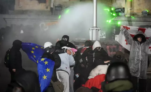 Demonstrators stand under running water from a fire-pump used by police rallying outside the parliament to continue protests against the government's decision to suspend negotiations on joining the European Union in Tbilisi, Georgia, on Tuesday, Dec. 3, 2024. (AP Photo/Pavel Bednyakov)