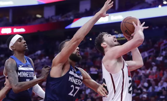 Houston Rockets center Alperen Sengun, right, puts up a shot in front of Minnesota Timberwolves forward Jaden McDaniels, left, and center Rudy Gobert (27) during the first half of an NBA basketball game Friday, Dec. 27, 2024, in Houston. (AP Photo/Michael Wyke)