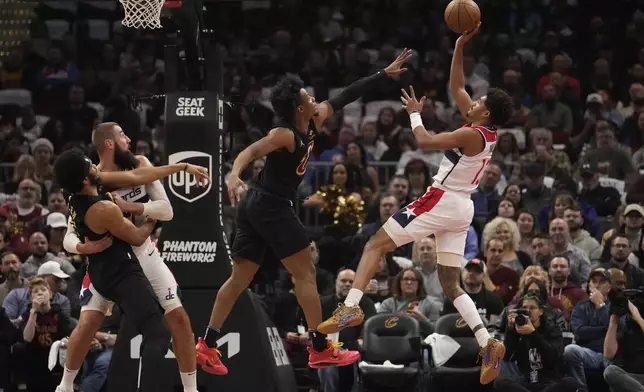 Washington Wizards guard Jordan Poole (13) shoots over Cleveland Cavaliers forward Isaac Okoro, center, in the first half of an NBA Cup basketball game, Tuesday, Dec. 3, 2024, in Cleveland. (AP Photo/Sue Ogrocki)