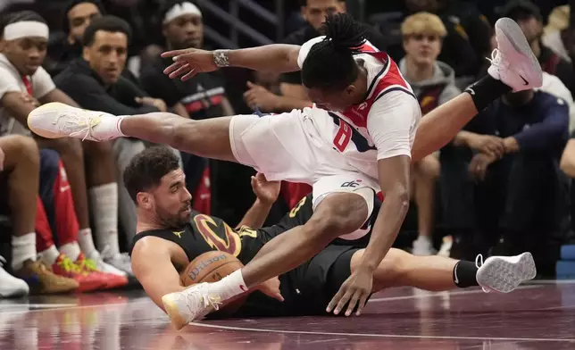 Washington Wizards guard Carlton Carrington tumbles over Cleveland Cavaliers forward Georges Niang, left, as they reach for a loose ball in the first half of an NBA Cup basketball game, Tuesday, Dec. 3, 2024, in Cleveland. (AP Photo/Sue Ogrocki)