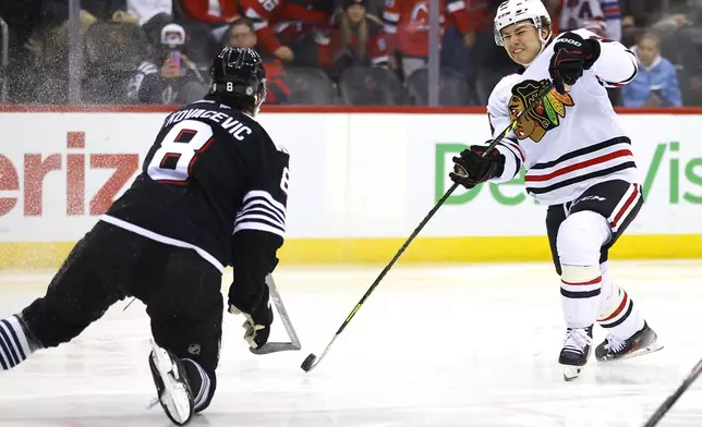 Chicago Blackhawks center Connor Bedard (98) shoots the puck as New Jersey Devils defenseman Johnathan Kovacevic (8) defends during the first period of an NHL hockey game, Saturday, Dec. 14, 2024, in Newark, N.J. (AP Photo/Noah K. Murray)