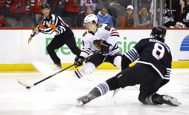 Chicago Blackhawks center Connor Bedard (98) plays the puck as New Jersey Devils defenseman Johnathan Kovacevic (8) defends during the first period of an NHL hockey game, Saturday, Dec. 14, 2024, in Newark, N.J. (AP Photo/Noah K. Murray)