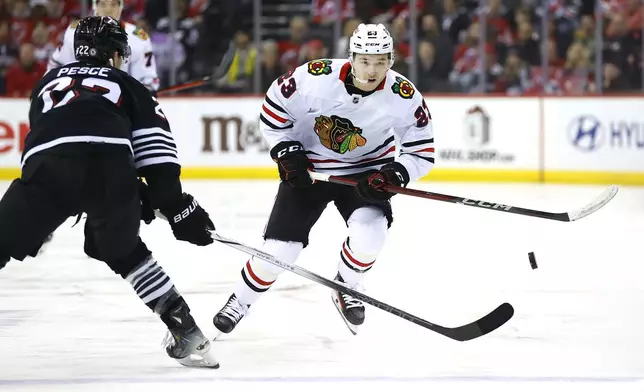 Chicago Blackhawks center Philipp Kurashev (23) plays the puck past New Jersey Devils defenseman Brett Pesce (22) during the first period of an NHL hockey game, Saturday, Dec. 14, 2024, in Newark, N.J. (AP Photo/Noah K. Murray)