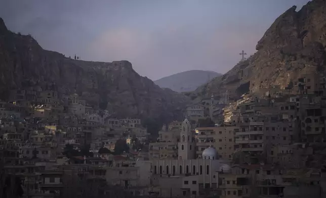 Houses are seen along the mountain as a cross stands over the Greek Orthodox convent Saint Takla on Christmas Eve in Maaloula, some 60 km northern Damascus, Syria, Tuesday, Dec. 24, 2024. (AP Photo/Leo Correa)