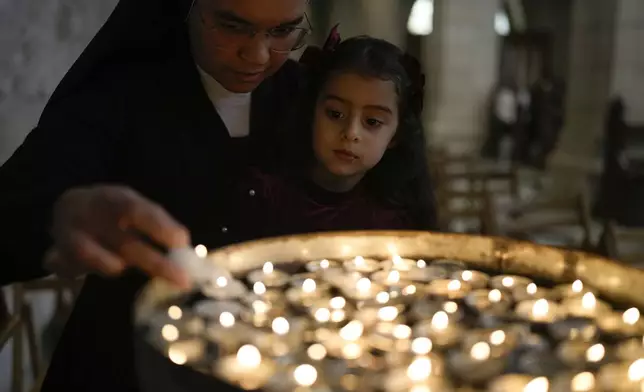 A nun holds a child to light a candle before the Christmas morning Mass at the Chapel of Saint Catherine, traditionally believed to be the birthplace of Jesus, in the West Bank city of Bethlehem, Wednesday, Dec. 25, 2024. (AP Photo/Matias Delacroix)