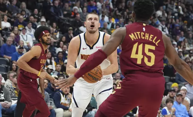 Denver Nuggets center Nikola Jokic drives between Cleveland Cavaliers center Jarrett Allen, left, and guard Donovan Mitchell, right, in the first half of an NBA basketball game Friday, Dec. 27, 2024, in Denver. (AP Photo/David Zalubowski)