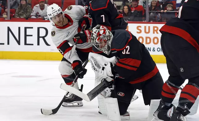 Carolina Hurricanes goaltender Pyotr Kochetkov (52) covers the puck as Ottawa Senators' Nick Jensen (3) looks around Dmitry Orlov (7) during the first period of an NHL hockey game in Raleigh, N.C., Friday, Dec. 13, 2024. (AP Photo/Karl B DeBlaker)