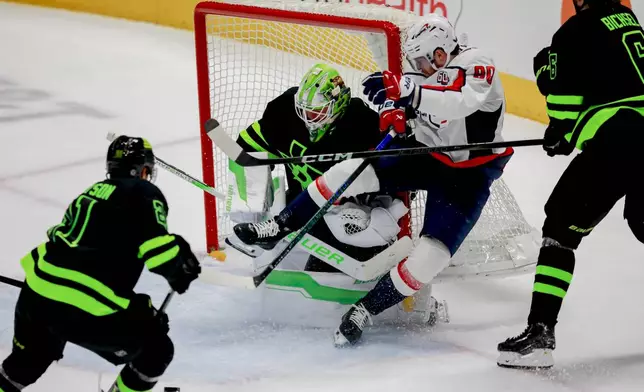 Washington Capitals left wing Pierre-Luc Dubois, center right, runs into Dallas Stars goaltender Jake Oettinger, center left, during the third period of an NHL hockey game in Dallas, Monday, Dec. 16, 2024. (AP Photo/Gareth Patterson)