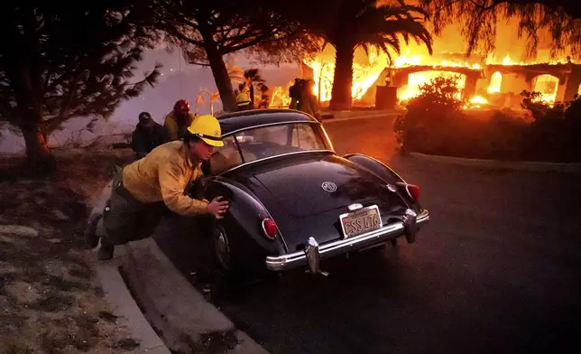 Firefighters and sheriff's deputies push a vintage car away from a burning home as the Mountain Fire burns in Camarillo, Calif., on Wednesday, Nov. 6, 2024. (AP Photo/Noah Berger)