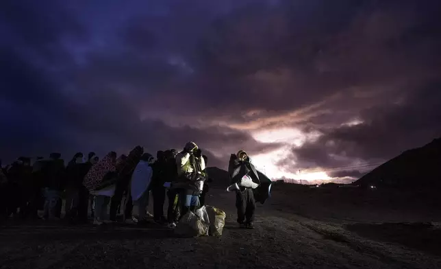 Asylum-seeking migrants wrap themselves in blankets to ward off the wind and rain as they line up in a makeshift, mountainous campsite to be processed after crossing the border with Mexico, Friday, Feb. 2, 2024, near Jacumba Hot Springs, Calif. (AP Photo/Gregory Bull)