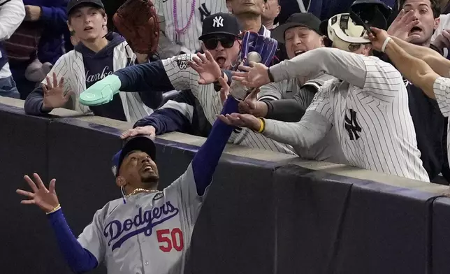 Fans interfere with a foul ball caught by Los Angeles Dodgers right fielder Mookie Betts during the first inning in Game 4 of the baseball World Series against the New York Yankees, Tuesday, Oct. 29, 2024, in New York. (AP Photo/Ashley Landis)