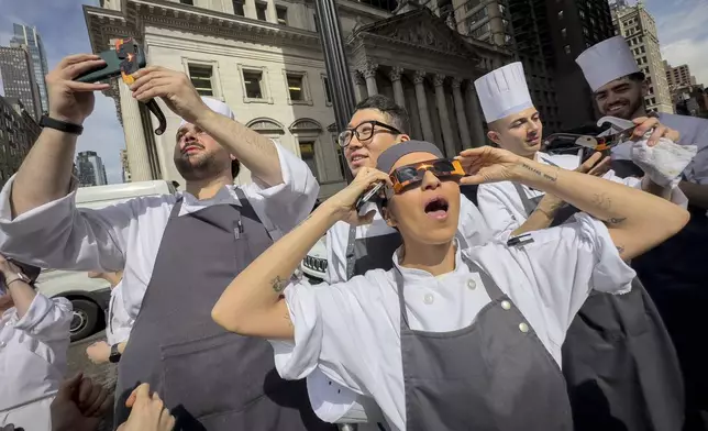 Restaurant workers in the Flatiron district of Manhattan take a break to view the solar eclipse, Monday, April 8, 2024, in New York. (AP Photo/John Minchillo)