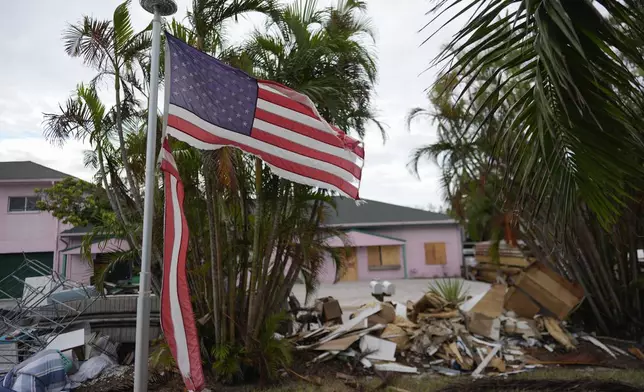 A tattered American flag flaps outside a home as furniture and household items damaged by Hurricane Helene flooding sit piled along the street awaiting pickup, ahead of the arrival of Hurricane Milton, in Holmes Beach on Anna Maria Island, Fla., Tuesday, Oct. 8, 2024. (AP Photo/Rebecca Blackwell)