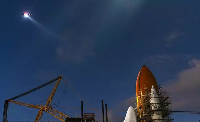 A helicopter beams a light on the tip of the fuel tanks of NASA's retired Space Shuttle Endeavour at the future Samuel Oschin Air and Space Center in Los Angeles, Friday, Feb. 2, 2024. (AP Photo/Damian Dovarganes)