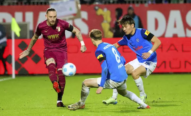 Augsburg's Marius Wolf, left, challenges for the ball with Kiel's Finn Porath, centre, and Shuto Machino during the Bundesliga soccer between Holstein Kiel and FC Augsburg in Kiel, Germany, Saturday, Dec. 21, 2024. (Frank Molter /dpa via AP)