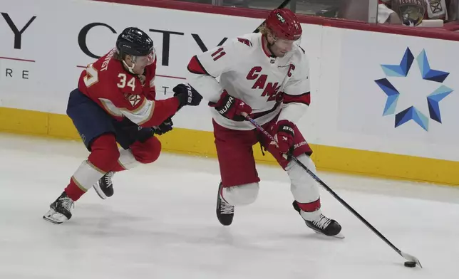 Florida Panthers defenseman Adam Boqvist (34) and Carolina Hurricanes center Jordan Staal (11) go after the puck during the first period of an NHL hockey game, Saturday, Nov. 30, 2024, in Sunrise, Fla. (AP Photo/Marta Lavandier)