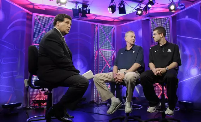 FILE - Greg Gumbel, left, watches as Connecticut head coach Jim Calhoun talks to Butler head coach Brad Stevens, right, prior to taping a television interview for the men's NCAA Final Four college basketball championship game Sunday, April 3, 2011, in Houston. (AP Photo/Eric Gay, File)