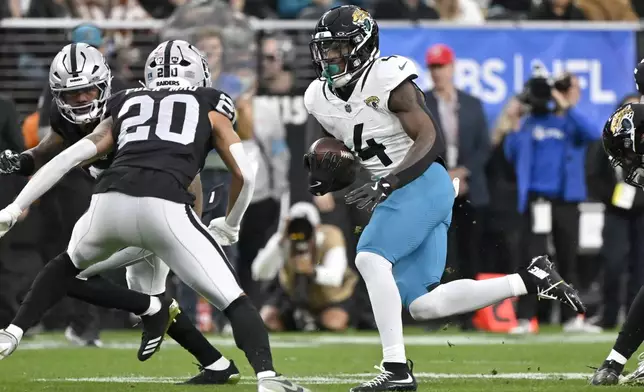 Jacksonville Jaguars running back Tank Bigsby (4) runs for a first down against the Las Vegas Raiders defense, including Raiders safety Isaiah Pola-Mao (20), during the first half of an NFL football game Sunday, Dec. 22, 2024, in Las Vegas. (AP Photo/David Becker)