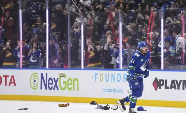 Hats litter the ice as Vancouver Canucks' Kiefer Sherwood (44) skates to the bench after scoring his third goal against the Colorado Avalanche, during the third period of an NHL hockey game in Vancouver, Monday, Dec. 16, 2024. (Darryl Dyck/The Canadian Press via AP)