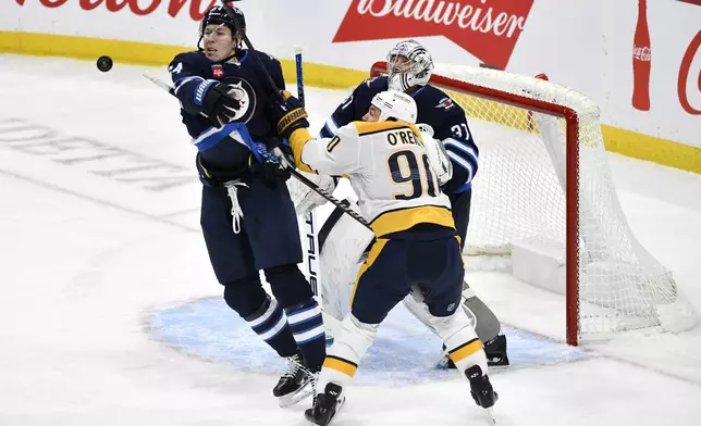 Winnipeg Jets' Logan Stanley reaches for a bouncing puck as he defends against Nashville Predators' Ryan O'Reilly in front of goaltender Connor Hellebuyck during the first period of an NHL hockey game in Winnipeg, Manitoba, Monday, Dec. 30, 2024. (Fred Greenslade/The Canadian Press via AP)