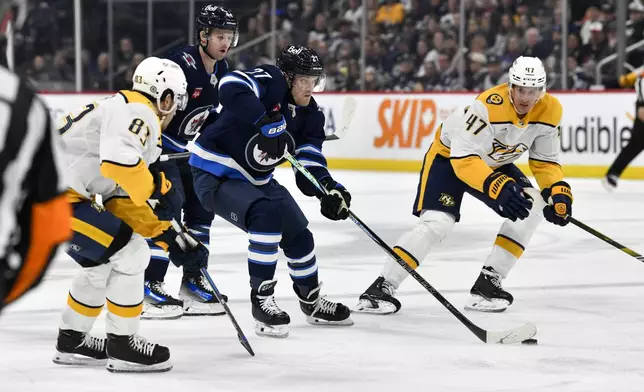 Winnipeg Jets' Nikolaj Ehlers (27) carries the puck past Nashville Predators' Adam Wilsby (83) and Michael McCarron (47) during the second period of an NHL hockey game in Winnipeg, Manitoba, Monday, Dec. 30, 2024. (Fred Greenslade/The Canadian Press via AP)