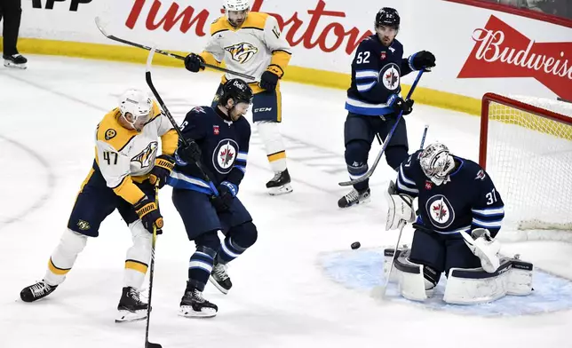 Winnipeg Jets goaltender Connor Hellebuyck makes a save on a shot by Nashville Predators' Michael McCarron (47) as he is defended by Colin Miller during the first period of an NHL hockey game in Winnipeg, Manitoba, Monday, Dec. 30, 2024. (Fred Greenslade/The Canadian Press via AP)