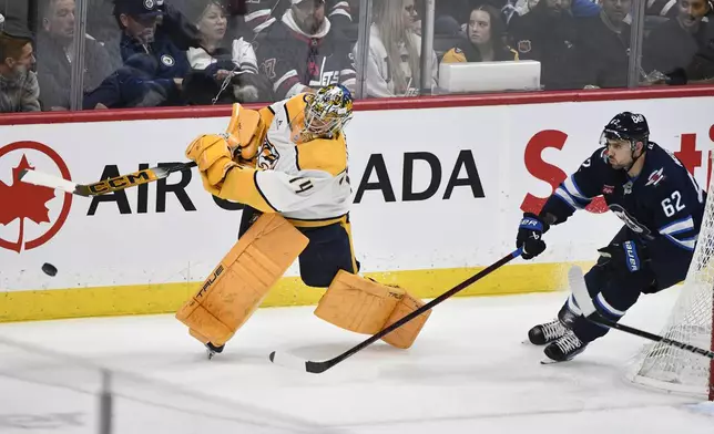 Nashville Predators goaltender Juuse Saros clears the puck from behind his net as he is pursued by Winnipeg Jets' Nino Niederreiter (62) during the first period of an NHL hockey game in Winnipeg, Manitoba, Monday, Dec. 30, 2024. (Fred Greenslade/The Canadian Press via AP)