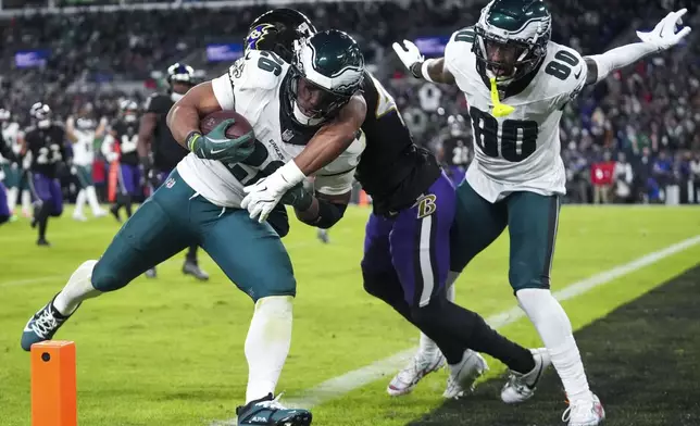 Philadelphia Eagles running back Saquon Barkley, left, is hit by Baltimore Ravens cornerback Marlon Humphrey, center, as Eagles wide receiver Parris Campbell (80) looks on during a touchdown run by Barkley in the second half of an NFL football game, Sunday, Dec. 1, 2024, in Baltimore. (AP Photo/Stephanie Scarbrough)