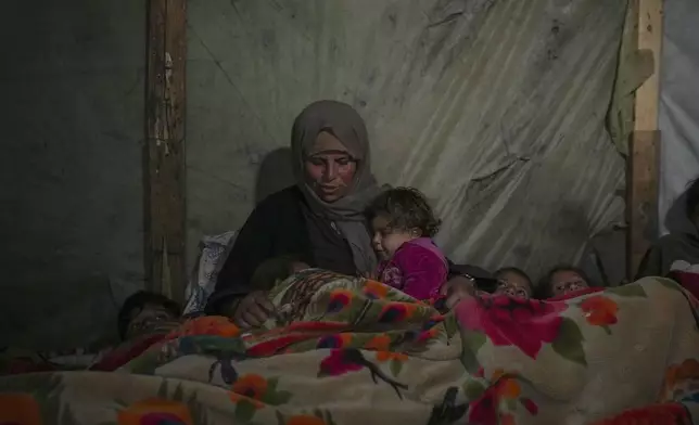 Reda Abu Zarada wraps herself and her grandchildren in blankets as they prepare to sleep in their tent at a camp in Khan Younis, Gaza Strip, Thursday Dec. 19, 2024. (AP Photo/Abdel Kareem Hana)