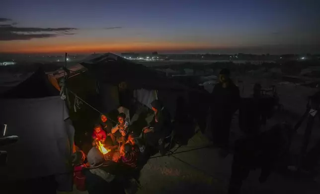 Reda Abu Zarada, 50, displaced from Jabaliya in nothern Gaza, sits by a fire with her grandchildren at a camp by the sea in Khan Younis, Gaza Strip, Thursday, Dec. 19, 2024. (AP Photo/Abdel Kareem Hana)