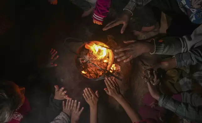 Reda Abu Zarada, 50, displaced from Jabaliya in northern Gaza, warms up by a fire with her grandchildren at a camp in Khan Younis, Gaza Strip, Thursday, Dec. 19, 2024. (AP Photo/Abdel Kareem Hana)