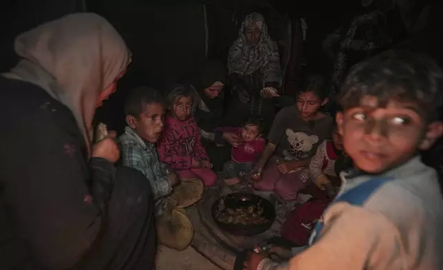 Amani Abu Zarada, fourth from left, feeds one of her children with fried zucchini made over a fire made of paper and cardboard scraps outside their tent in a camp in Khan Younis, Gaza Strip, Thursday, Dec. 19, 2024. (AP Photo/Abdel Kareem Hana)