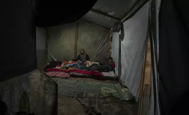 Reda Abu Zarada wraps herself and her grandchildren in blankets as they prepare to sleep in their tent at a camp in Khan Younis, Gaza Strip, Thursday, Dec. 19, 2024. (AP Photo/Abdel Kareem Hana)