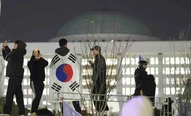 A man wearing a national flag stands on the wall of the National Assembly in Seoul, South Korea, Wednesday, Dec. 4, 2024. (AP Photo/Lee Jin-man)