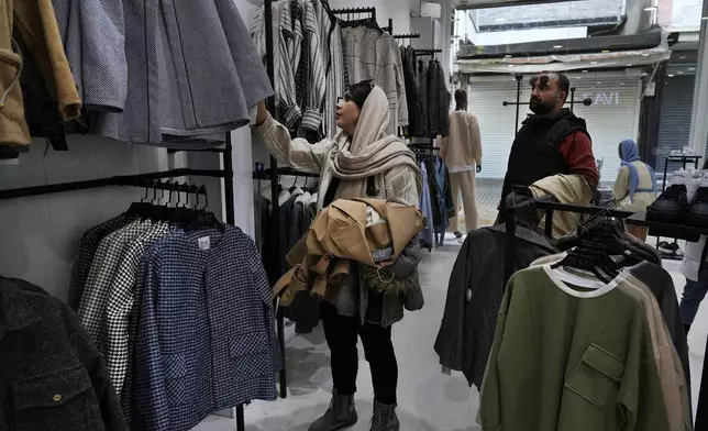 A woman selects clothes as her husband looks on at a shop in port city of Bandar Anzali in northern Iran, Thursday, Dec. 5, 2024. (AP Photo/Vahid Salemi)