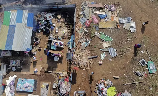 People walk by destroyed homes in the Barakani, Mayotte, informal settlement, Saturday, Dec. 21, 2024. (AP Photo/Adrienne Surprenant)