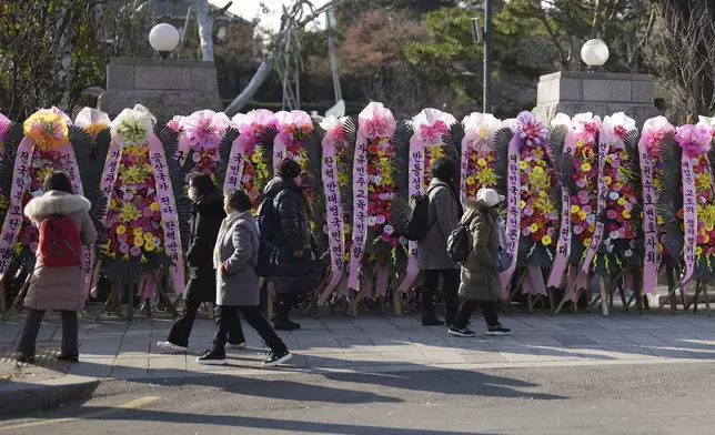 People walk past wreaths sent by supporters of impeached South Korean President Yoon Suk Yeol outside of the Constitutional Court in Seoul, South Korea, Tuesday, Dec. 17, 2024. (AP Photo/Lee Jin-man)