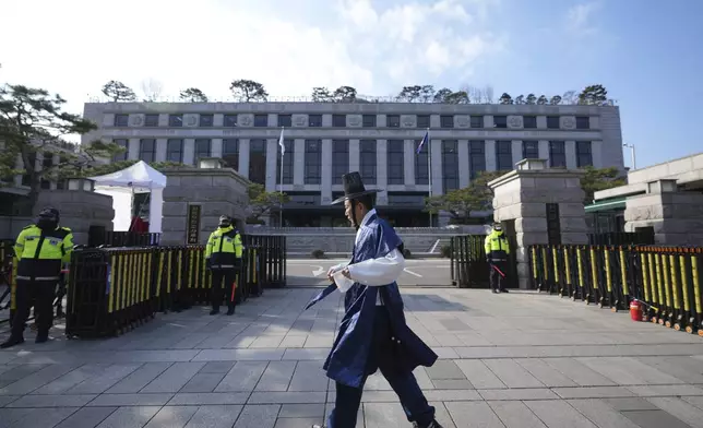 A visitor wearing South Korean traditional costume "Hanbok" walks past in front of the Constitutional Court in Seoul, South Korea, Tuesday, Dec. 17, 2024. (AP Photo/Lee Jin-man)