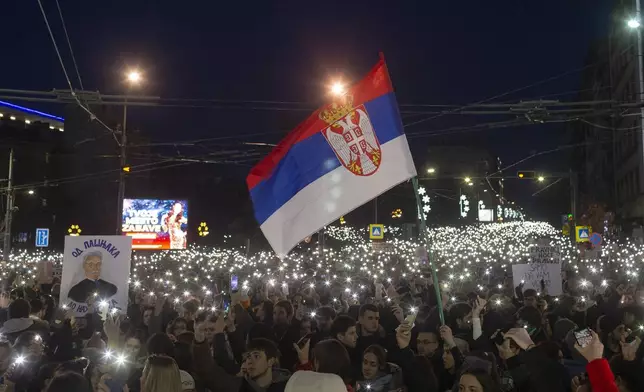 A Serbian flag waves in the wind as people use lights on their mobile phones during a protest against populist President Aleksandar Vucic and his government, whose tight grip on power has been challenged by weeks of street protests led by university students, in Belgrade, Serbia, Sunday, Dec. 22, 2024. (AP Photo/Marko Drobnjakovic)