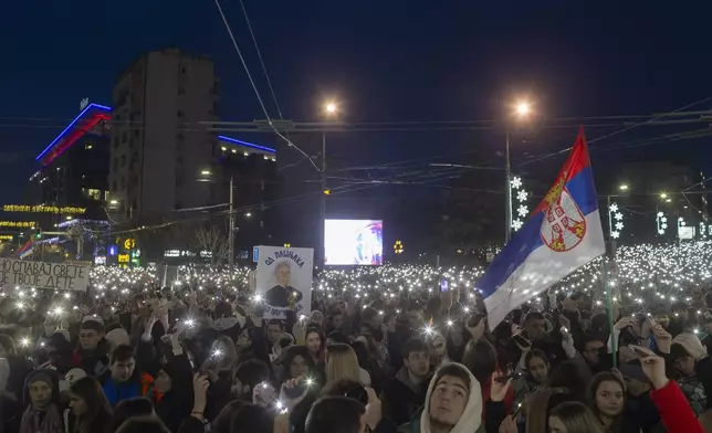 A Serbian flag is seen as people use lights on their mobile phones during a protest against President Aleksandar Vucic and his government, in Belgrade, Serbia, Sunday, Dec. 22, 2024. (AP Photo/Marko Drobnjakovic)