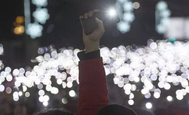 People use lights on their mobile phones during a protest against populist President Aleksandar Vucic and his government, whose tight grip on power has been challenged by weeks of street protests led by university students, in Belgrade, Serbia, Sunday, Dec. 22, 2024. (AP Photo/Marko Drobnjakovic)