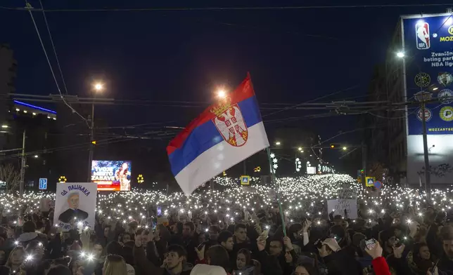 A Serbian flag waves in the wind as people use lights on their mobile phones during a protest against populist President Aleksandar Vucic and his government, whose tight grip on power has been challenged by weeks of street protests led by university students, in Belgrade, Serbia, Sunday, Dec. 22, 2024. (AP Photo/Marko Drobnjakovic)