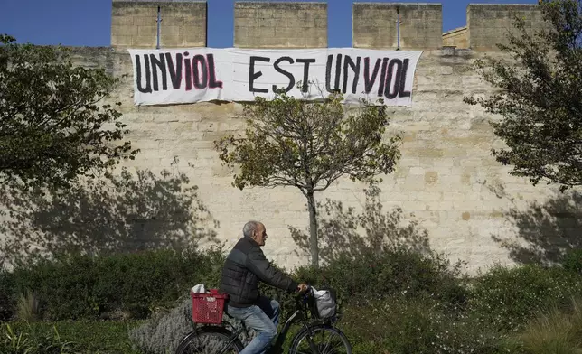 FILE - A man rides a bicycle in front of a banner that reads, "A rape is a rape," in Avignon, southern France, on Oct. 16, 2024. (AP Photo/Lewis Joly, File)