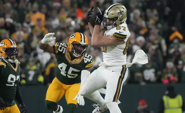 New Orleans Saints tight end Foster Moreau (87) pulls in a pass against Green Bay Packers linebacker Eric Wilson (45) during the first half of an NFL football game, Monday, Dec. 23, 2024, in Green Bay, Wis. (AP Photo/Morry Gash)