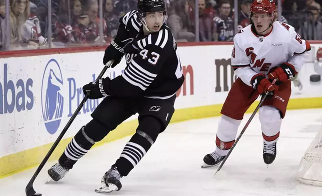 New Jersey Devils defenseman Luke Hughes (43) controls the puck past Carolina Hurricanes forward Jackson Blake, right, in the second period of an NHL hockey game Friday, Dec. 27, 2024, in Newark, N.J. (AP Photo/Adam Hunger)