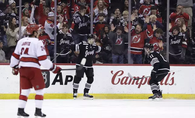 New Jersey Devils center Nico Hischier is congratulated by Stefan Noesen (11) after scoring a goal in the first period of an NHL hockey game in front of Carolina Hurricanes center Seth Jarvis (24) Friday, Dec. 27, 2024, in Newark, N.J. (AP Photo/Adam Hunger)