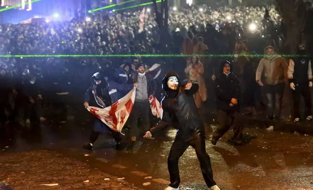 A masked demonstrator throws an object toward police during a rally against the governments' decision to suspend negotiations on joining the European Union for four years, outside the parliament's building in Tbilisi, Georgia, on Sunday, Dec. 1, 2024. (AP Photo/Zurab Tsertsvadze)