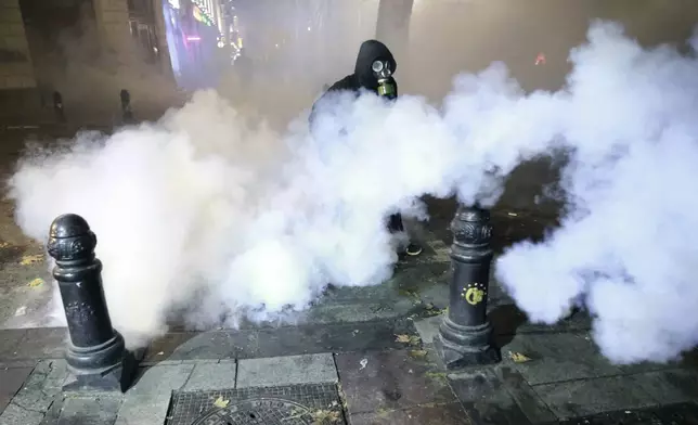 A demonstrator walks through a cloud of tear gas during a rally to protest against the government's decision to suspend negotiations on joining the European Union in Tbilisi, Georgia, early Wednesday, Dec. 4, 2024. (AP Photo/Zurab Tsertsvadze)