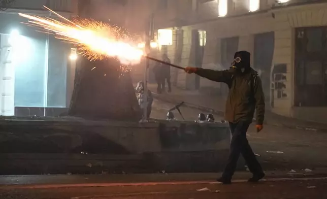 A demonstrator launches a firecracker towards the police during a rally to protest against the government's decision to suspend negotiations on joining the European Union in Tbilisi, Georgia, early Wednesday, Dec. 4, 2024. (AP Photo/Pavel Bednyakov)