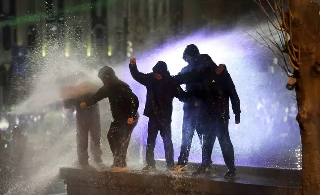 Demonstrators stand atop of a tomb under running water from a water cannon during a protests against the government's decision to suspend negotiations on joining the European Union, outside the parliament's building in Tbilisi, Georgia, on Monday, Dec. 2, 2024. (AP Photo/Zurab Tsertsvadze)